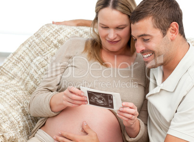 Adorable couple looking at an echography sitting on a couch