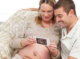 Adorable couple looking at an echography sitting on a couch