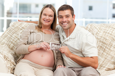 Cheerful couple of future parents holding an echography