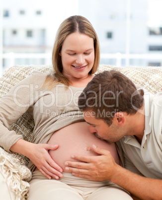 Proud man kissing the belly of his pregnant girlfriend sitting i