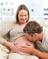 Proud man kissing the belly of his pregnant girlfriend sitting i