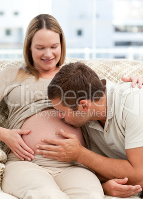 Attentive man kissing his wife's belly while relaxing on the sof