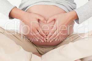 Close up of a pregnant woman doing heart sign on her belly