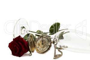 alte taschenuhr und eine rote rose unter einem liegenden leeren sektglas