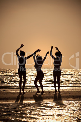 Three Young Women Dancing On Beach At Sunset