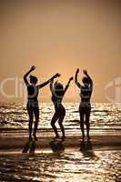 Three Young Women Dancing On Beach At Sunset