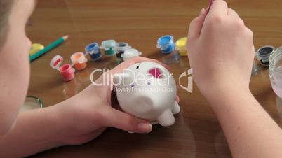 girl paints pig-coin box.