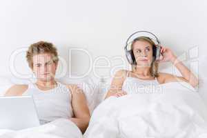 Young couple relax in bed with music and laptop