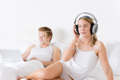 Young couple relax in bed with music and laptop