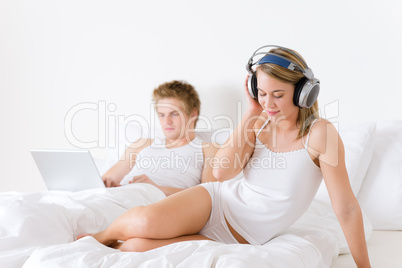 Young couple relax in bed with music and laptop