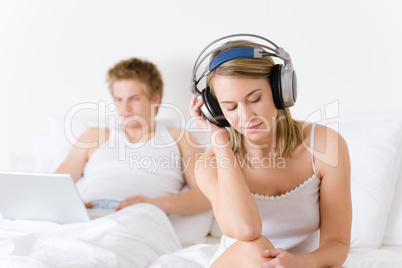 Young couple relax in bed with music and laptop