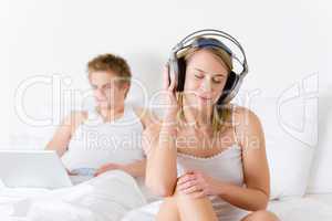Young couple relax in bed with music and laptop
