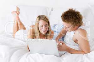 Young couple relax in bed with laptop lying down