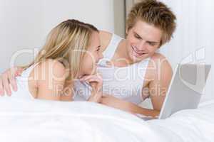 Young couple relax in bed with laptop