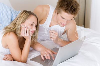 Young couple relax in bed with laptop