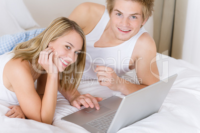 Young couple relax in bed with laptop