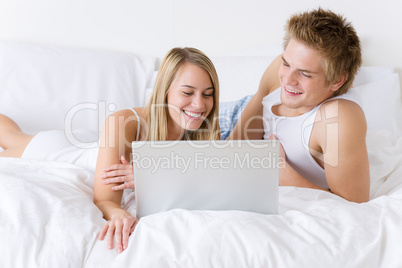 Young couple relax in bed with laptop lying down