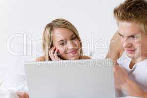 Young couple relax in bed with laptop lying down