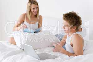 Young couple relax in bed with laptop and book