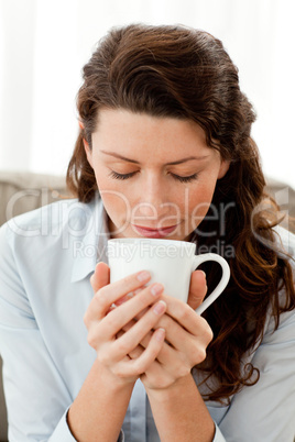 Pretty businesswoman smelling her coffee sitting on the sofa