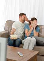 Lovely couple hiding their face from a horror movie sitting in t