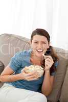 Portrait of a happy woman eating pop corn while watching televis