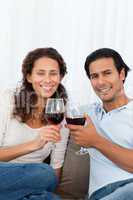 Happy couple clinking glasses of red wine on the sofa