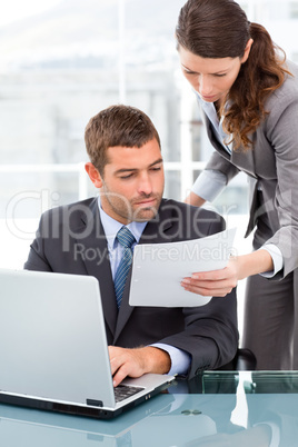 Two business people looking at a paper while working on the lapt