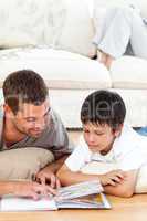 Attentive father reading a book with his son lying on the floor