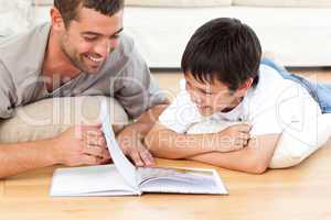 Cute boy reading a book with his father on the floor