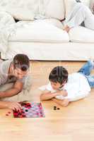 Father and son playing checkers together lying on the floor