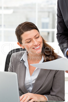 Happy businesswoman reading a paper while working on laptop