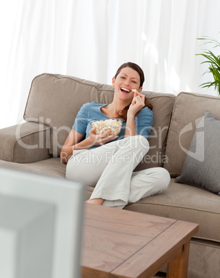 Cheerful woman watching television and eating pop corn