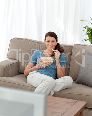 Happy woman eating pop corn while watching television on the sof