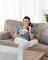 Happy woman eating pop corn while watching television on the sof