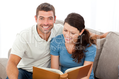 Pretty woman reading a book with her boyfriend on the sofa