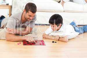 Handsome man playing checkers with his son lying on the floor