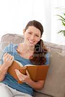 Happy woman holding a book sitting on her sofa