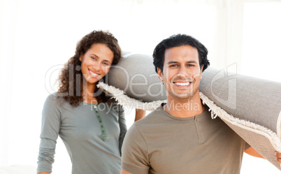 Cute couple carrying a carpet standing in the living room
