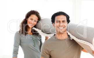 Cute couple carrying a carpet standing in the living room