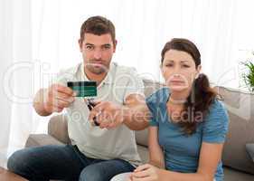 Worried couple cutting their credit card together sitting on the