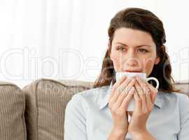 Pensive woman drinking coffee in the living room