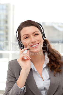 Cheerful businesswoman using earpiece sitting at her desk