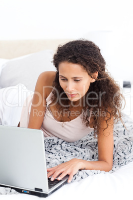 Pretty woman working on her laptop lying on her bed