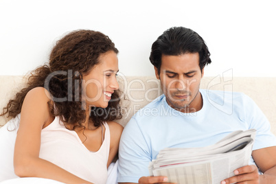 Happy woman looking at her serious boyfriend reading the newspap