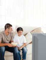 Happy boy watching television with his father on the sofa