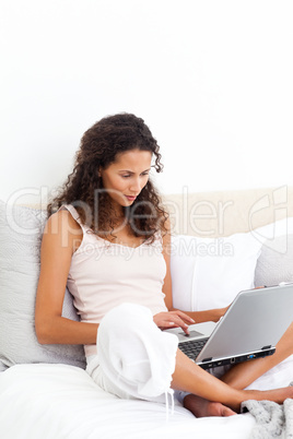 Attractive woman working on her laptop sitting on her bed