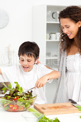Cute boy mixing a salad with his mother in the kitchen
