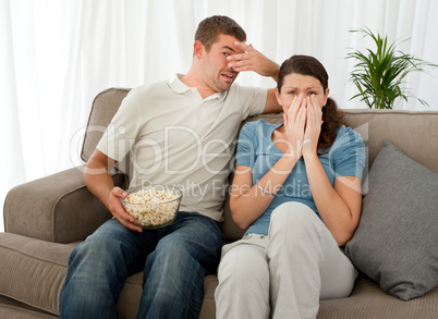 Scared couple eating pop corn while watching a horror movie