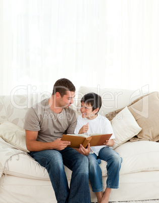 Adorable boy looking at a photo album with his father on the sof